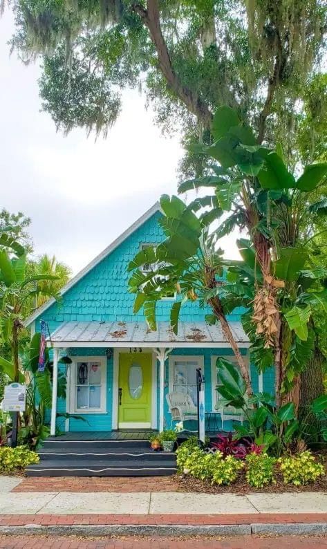 a blue house with green trim and trees around the front door is surrounded by greenery