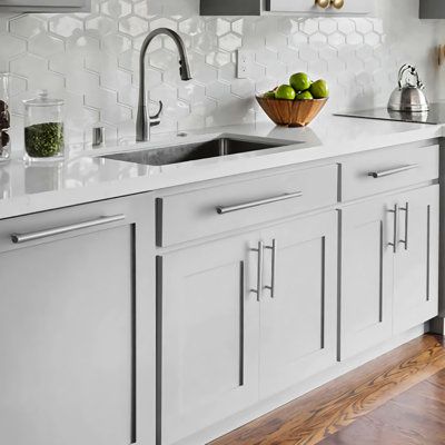 a white kitchen with wooden floors and stainless steel appliances on the countertop, along with two bowls of fruit