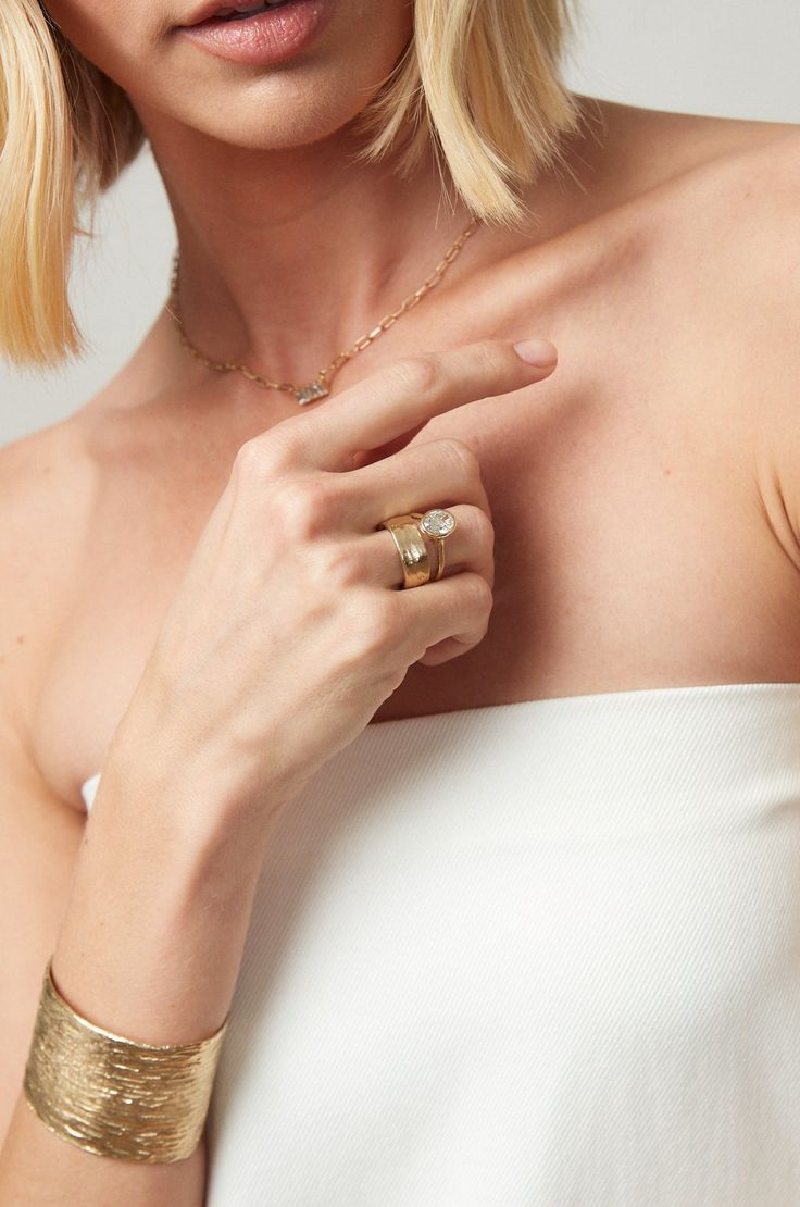 a woman in a white dress wearing a gold bracelet with two rings on her left hand