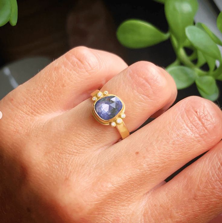 This stunning ring features a vibrant organic rose cut blue sapphire, highlighted with two side trios of sparkling white diamonds. The 22k gold bezel is set on a 3mm 18k gold band. The center stone measures approximately 1/3 inch x 1/2 inch. Matte finish. Luxury Minimalist Sapphire Ring With Bezel Setting, Heirloom Sapphire Ring With Bezel Setting, 14k Gold Sapphire Ring With Bezel Setting, Luxury Gold Sapphire Ring With Smooth Bezel, Heirloom Three-stone Sapphire Ring In 14k Gold, Blue Sapphire Ring, Hammered Band, Lovely Ring, Blue Sapphire Rings