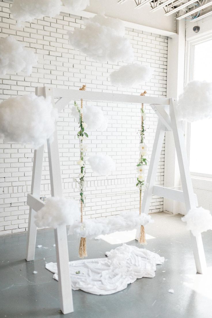 a white room with clouds hanging from the ceiling and flowers in vases on the floor