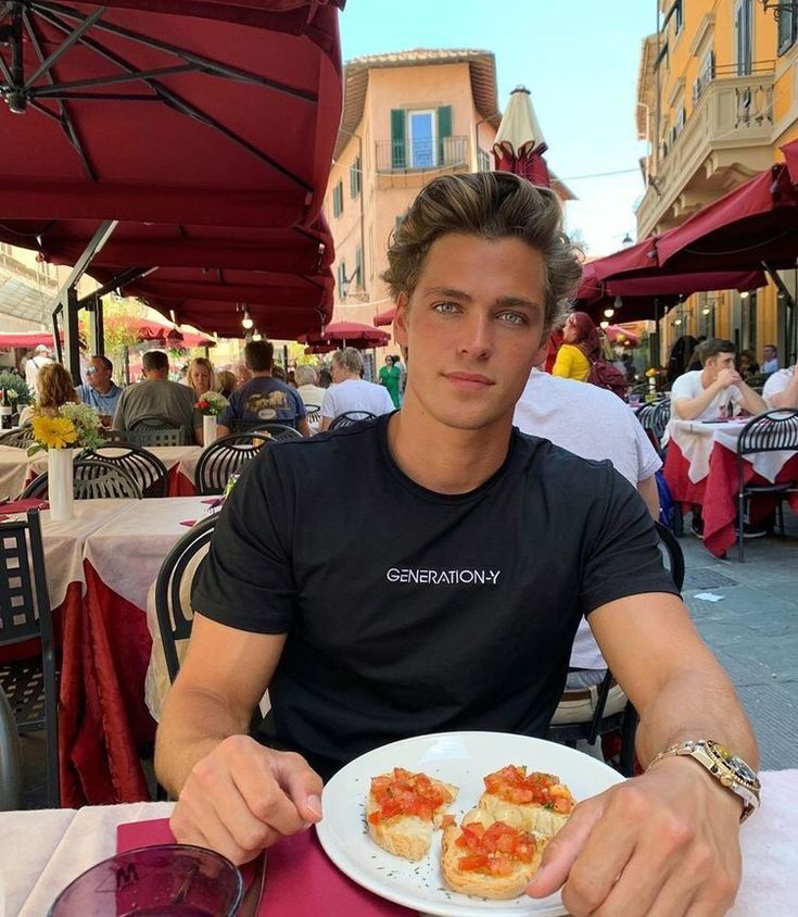 a man sitting at an outdoor table with food in front of him and looking into the camera