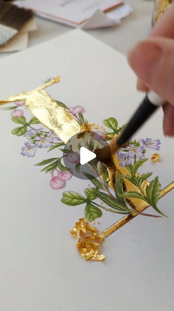 someone is painting flowers on a piece of paper with gold leaf trimmings and using a paintbrush