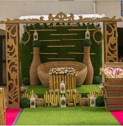 an outdoor stage set up with grass and flowers on the ground, surrounded by wicker furniture