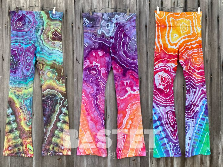 three pairs of colorful leggings hanging on a wooden fence next to each other