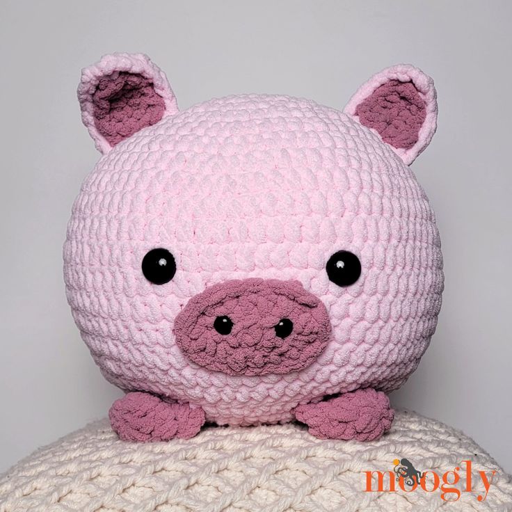 a pink crocheted pig sitting on top of a white pillow with black eyes