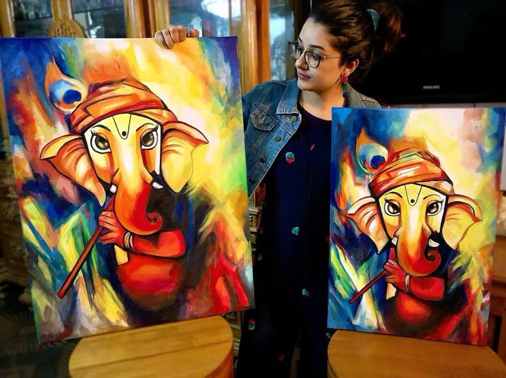 a woman standing next to two paintings on easels in front of a wooden table