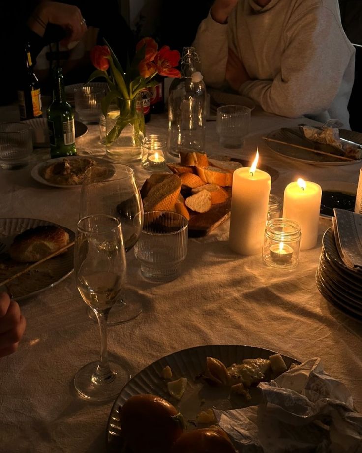 people sitting at a table with food and candles in front of the dinner plates on the table