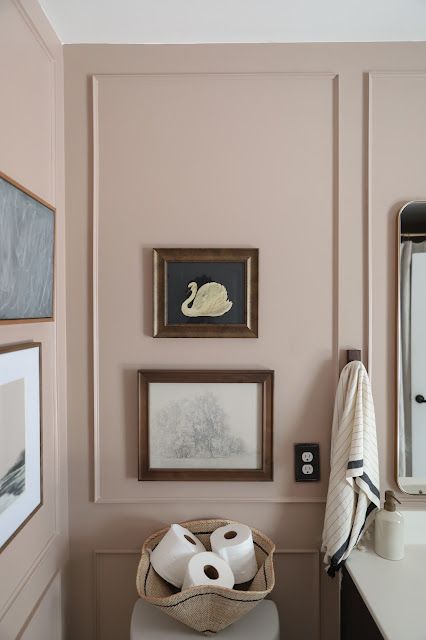 a bathroom with pink walls and pictures on the wall, toilet paper rolls in a basket