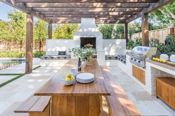 an outdoor kitchen and dining area with wood table, grilling oven, and benches