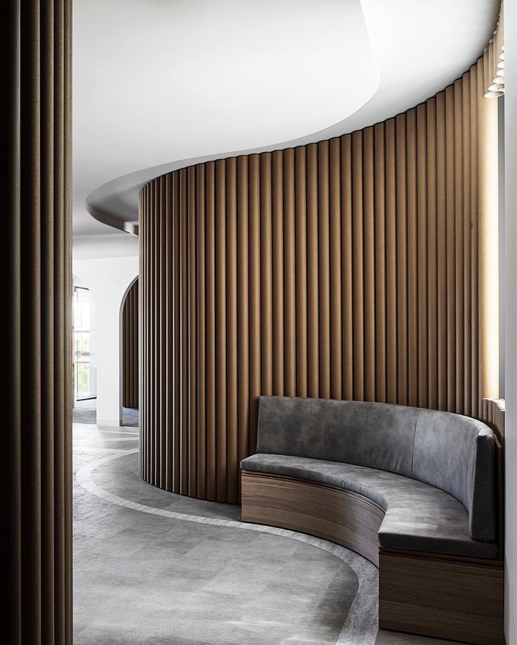 a curved couch sitting in the middle of a living room next to a wall with wooden slats on it