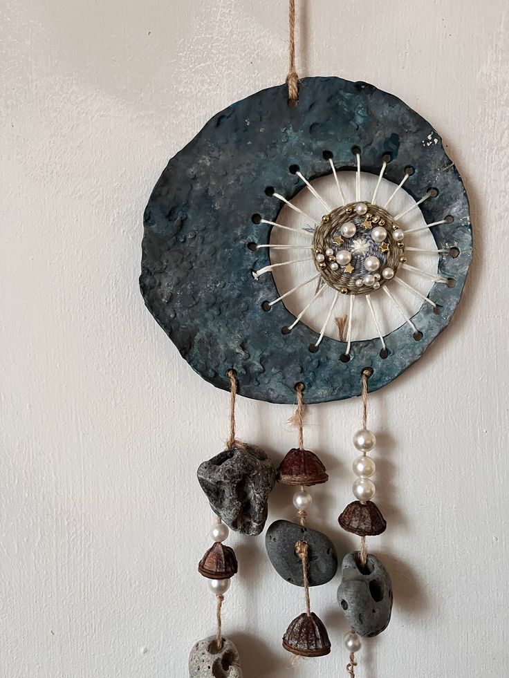 a decorative wall hanging with stones and beads on it's side, in the shape of a disc