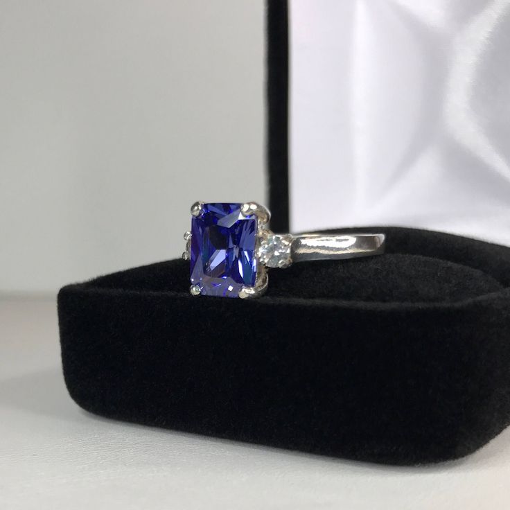 Beautiful Tanzanite* & White Sapphire Ring * 2.25ct Emerald Cut Violet Blue Tanzanite* measures 9mm x 7mm * 3.5mm Brilliant Cut White Sapphire Accents * 2.5cts Total weight * 14k White Gold * Size 9 Hallmarked & Gift Ready! Matching Earrings & Pendant Necklace is also Available! *Tanzanite is one of very few gemstones that cannot be grown in a Lab, however, these Laboratory Grown Simulate Stones are optically identical to a natural Tanzanite in color and are just as hard but, do not Classic Sapphire Gemstones With Accent Stones, Blue Radiant Cut Cubic Zirconia Rings, Tanzanite Gemstone With Center Stone As Gift, Sapphire Radiant Cut Ring With Accent Stones, Sapphire Ring With Radiant Cut And Accent Stones, Sapphire Center Stone Jewelry For Proposal, Tanzanite Gemstones Perfect For Gifts, Princess Cut Lab-created Sapphire Jewelry With Center Stone, Blue Radiant Cut Lab-created Sapphire Jewelry