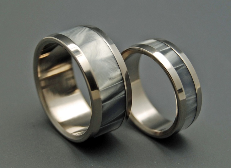 two wedding bands with silver inlays are shown on a gray surface and one is made out of metal