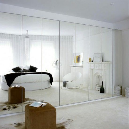 a large mirror in the middle of a room next to a white bed and ottoman