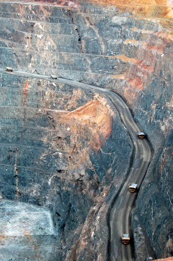 two trucks driving down the road in front of a large rock formation with steep sides