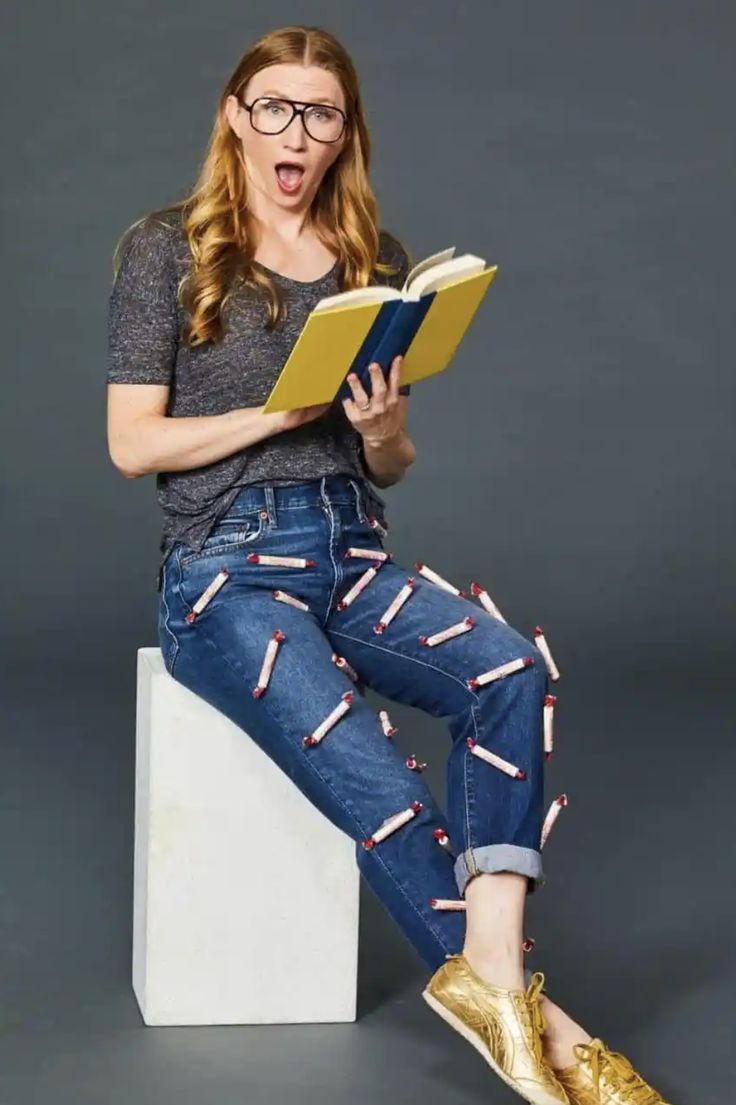 a woman sitting on top of a white block holding a book in her hand and reading