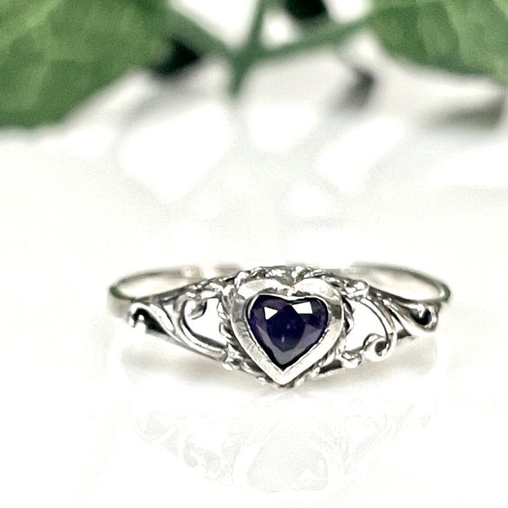 a heart shaped ring sitting on top of a white table next to green leafy leaves