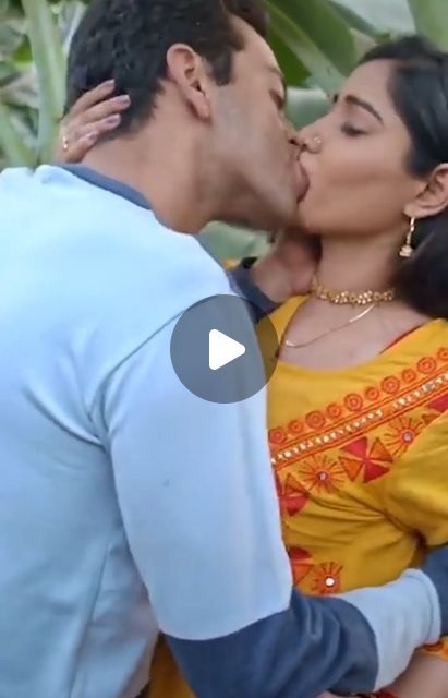 a man and woman kissing each other while standing next to each other in front of plants