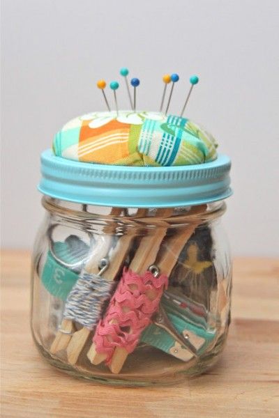 a jar filled with pins and needles on top of a wooden table