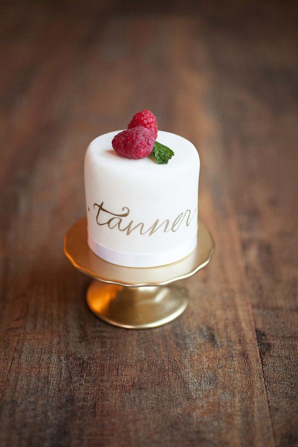 a small white cake topped with raspberries on top of a gold plated stand