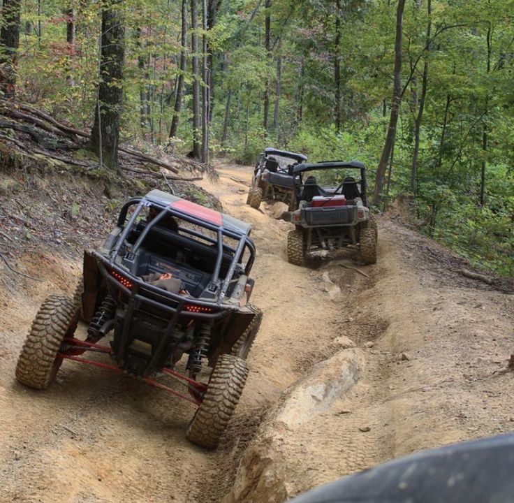 two people riding four wheelers on a dirt trail