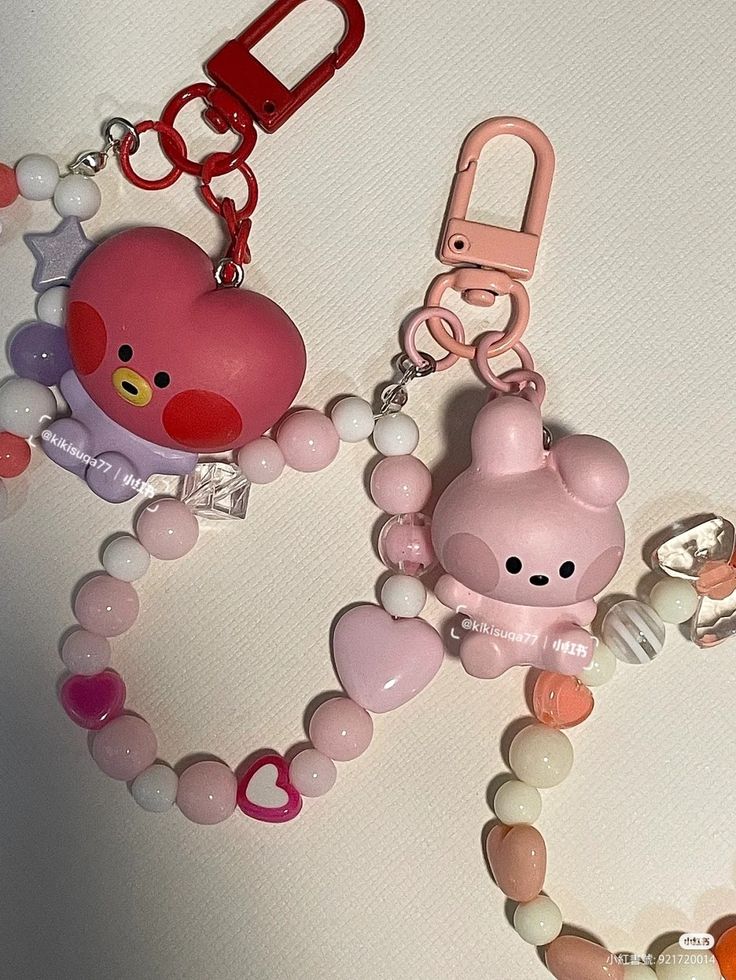 two keychains with charms attached to them on a white surface, one is pink and the other is red