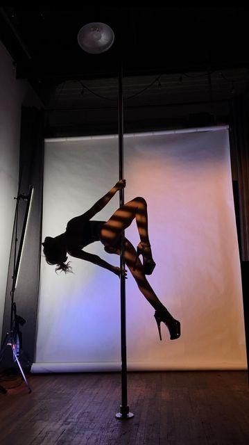 a woman is doing pole dancing on the floor in front of a white wall and lights