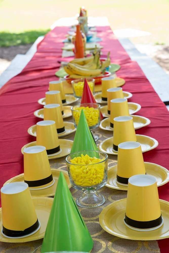 a long table with yellow and green hats on it's head, surrounded by party decorations