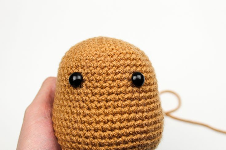 a hand holding a small brown crocheted object with black eyes on it's face