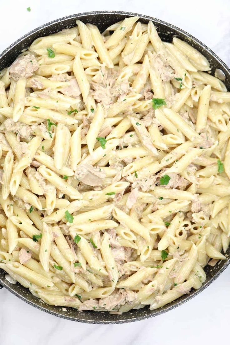 pasta with tuna and parsley in a skillet on a marble counter top, ready to be cooked