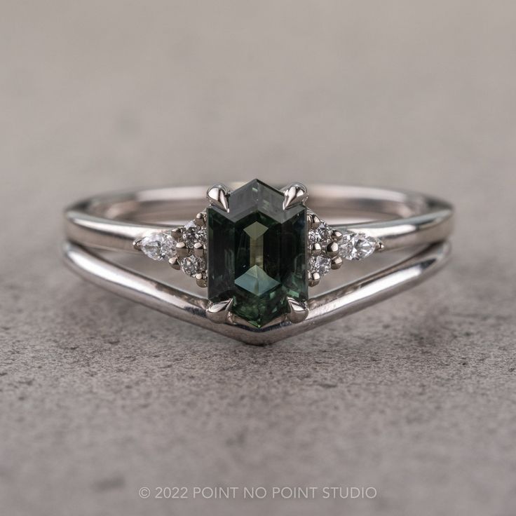 a green and white diamond ring sitting on top of a gray surface with diamonds around it