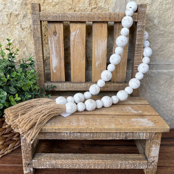 a wooden bench sitting next to a plant and a white beaded necklace on top of it