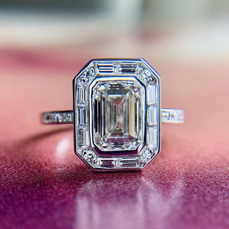 an emerald cut diamond ring sitting on top of a purple surface with diamonds around it