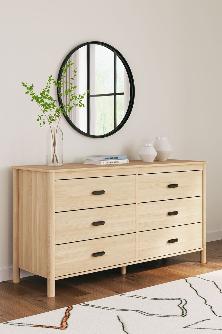 a wooden dresser with a round mirror above it and a plant in the vase on top