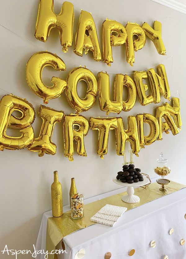 a table topped with gold foil balloons that say happy golden birthday written on the wall