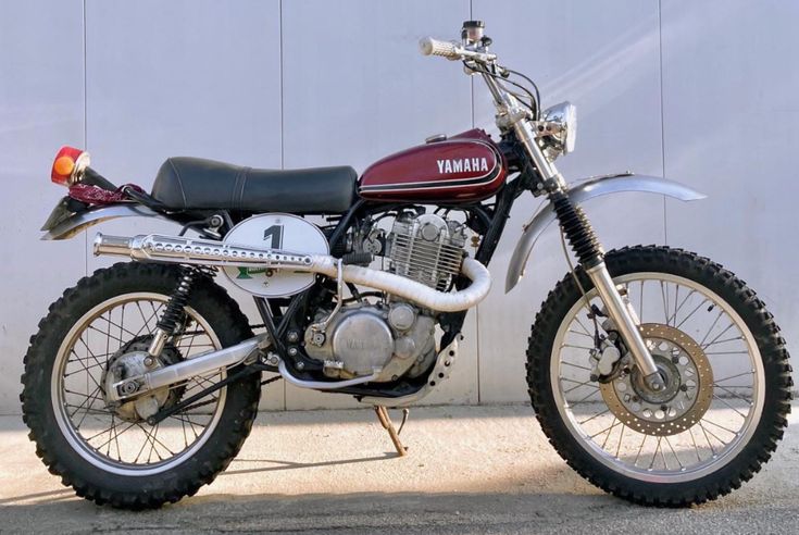 a red and white yamaha motorcycle parked in front of a building with a wall behind it