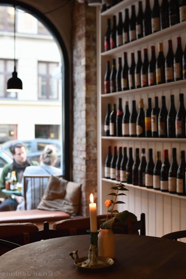 a table with a candle on it in front of a wall of bottles and chairs