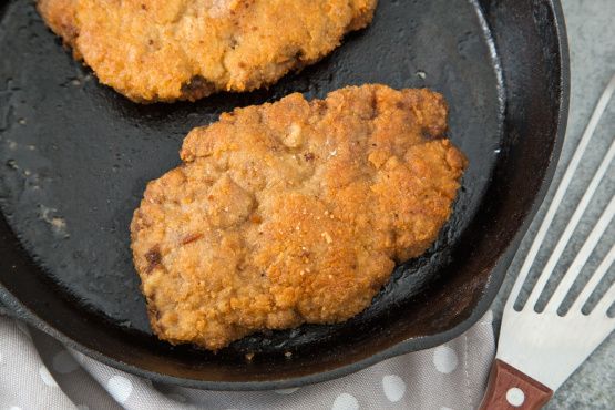 two fried meat patties in a frying pan next to a knife and fork