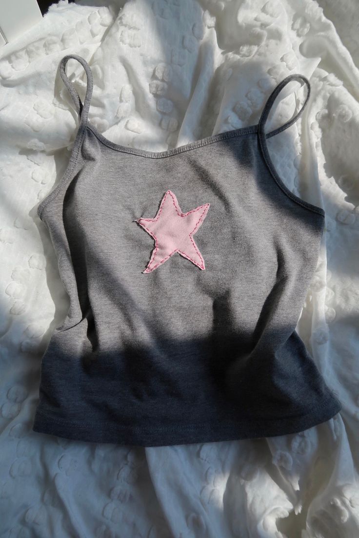 a gray and pink top with a star on the front sitting on a white sheet