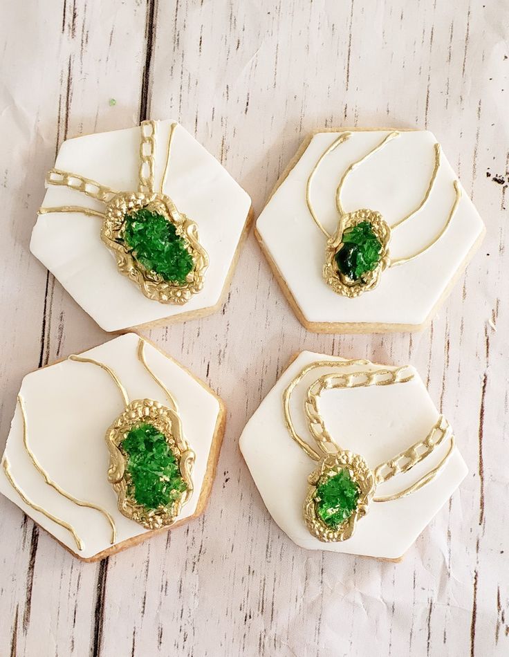 four cookies with green decorations on them sitting on a white plate and some gold chains