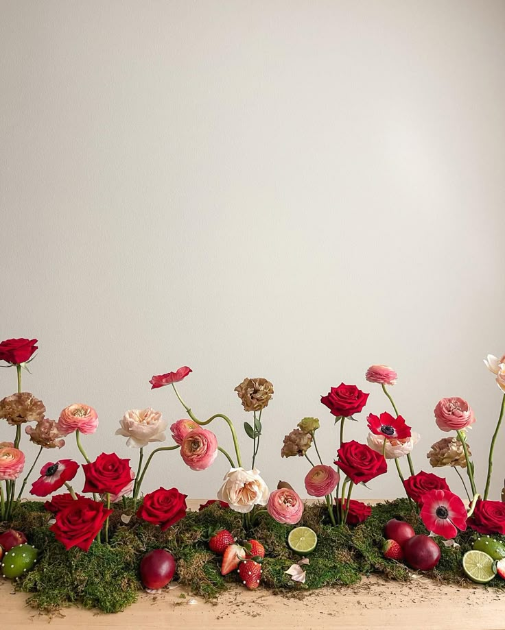 an arrangement of flowers on a table with moss and other things in the background,