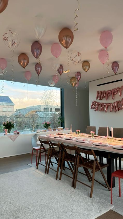 a dining room table with pink and gold balloons hanging from it's ceiling above