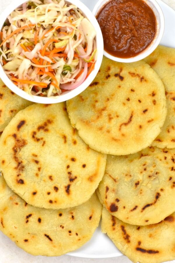 several flat breads on a plate with sauce and coleslaw in the bowl