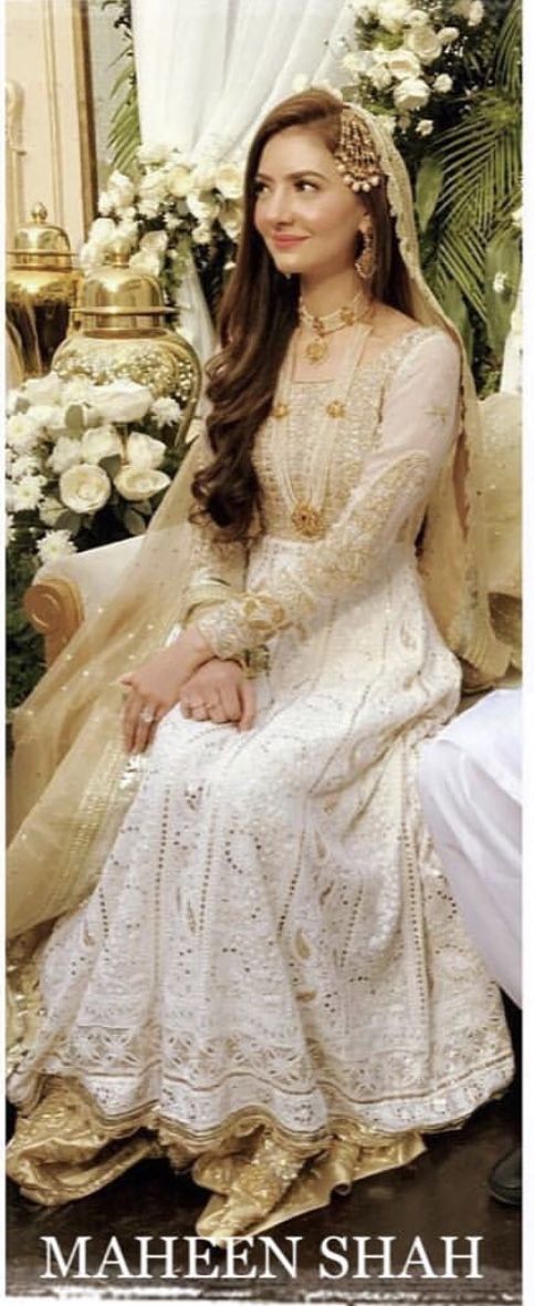 a woman sitting on top of a bed wearing a white dress and gold headpiece