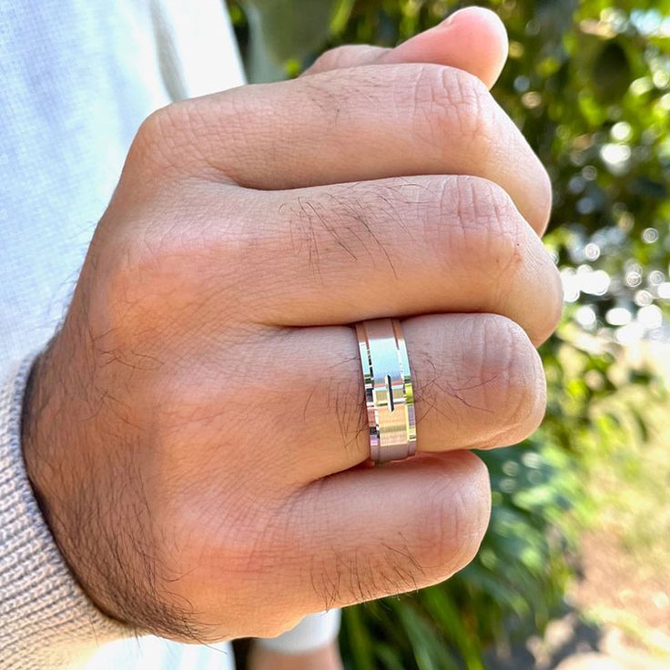 a man's hand with a ring on it that is in front of some bushes