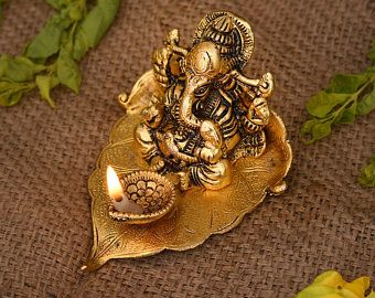 an elephant figurine sitting on top of a leaf with a candle in its mouth