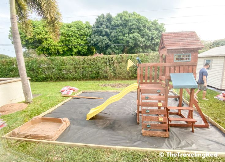 there is a wooden play set in the back yard with a slide and sandpit