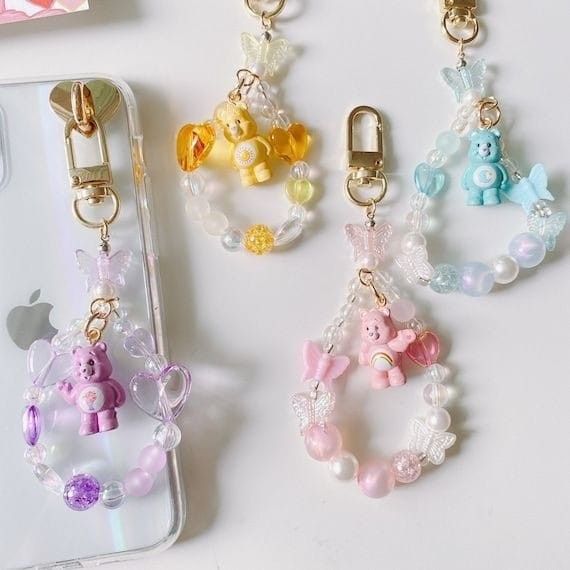 four cell phones with charms attached to them sitting on a table next to an iphone