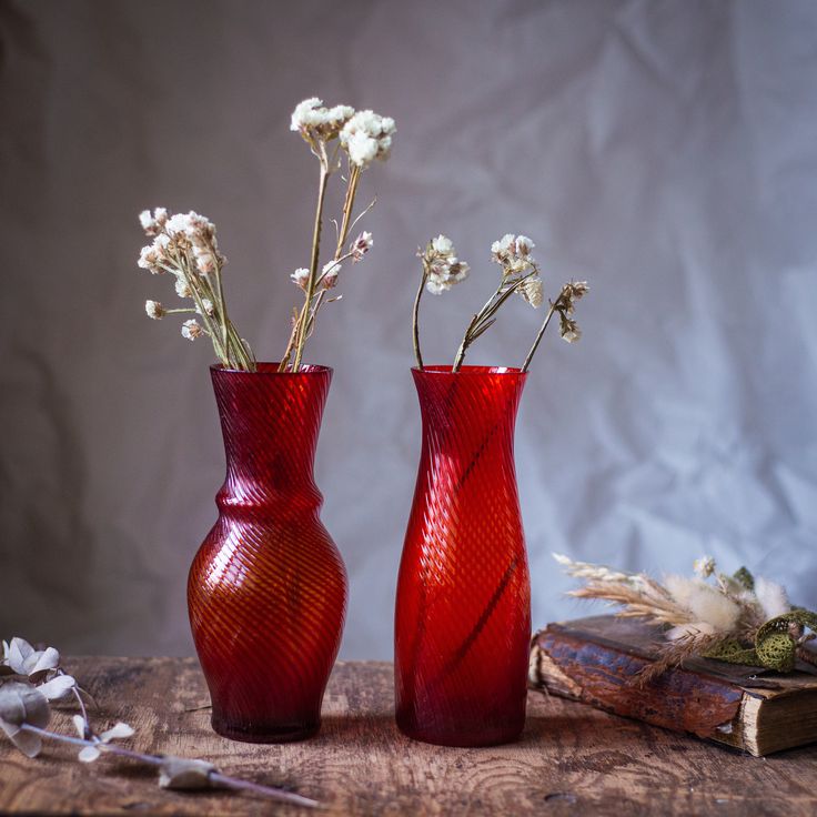 two red vases sitting on top of a wooden table next to books and dried flowers